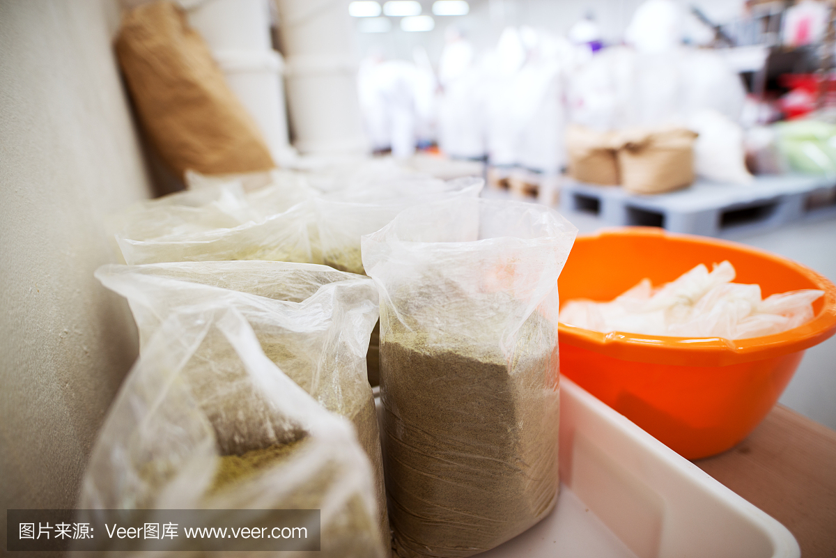 在食品生产厂的橙色塑料盆旁,近距离观察装满绿色香料的塑料透明袋。